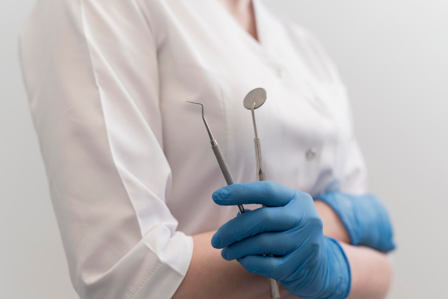 Стоматолог в медицинских перчатках держит стоматологические инструменты — зеркало и зонд